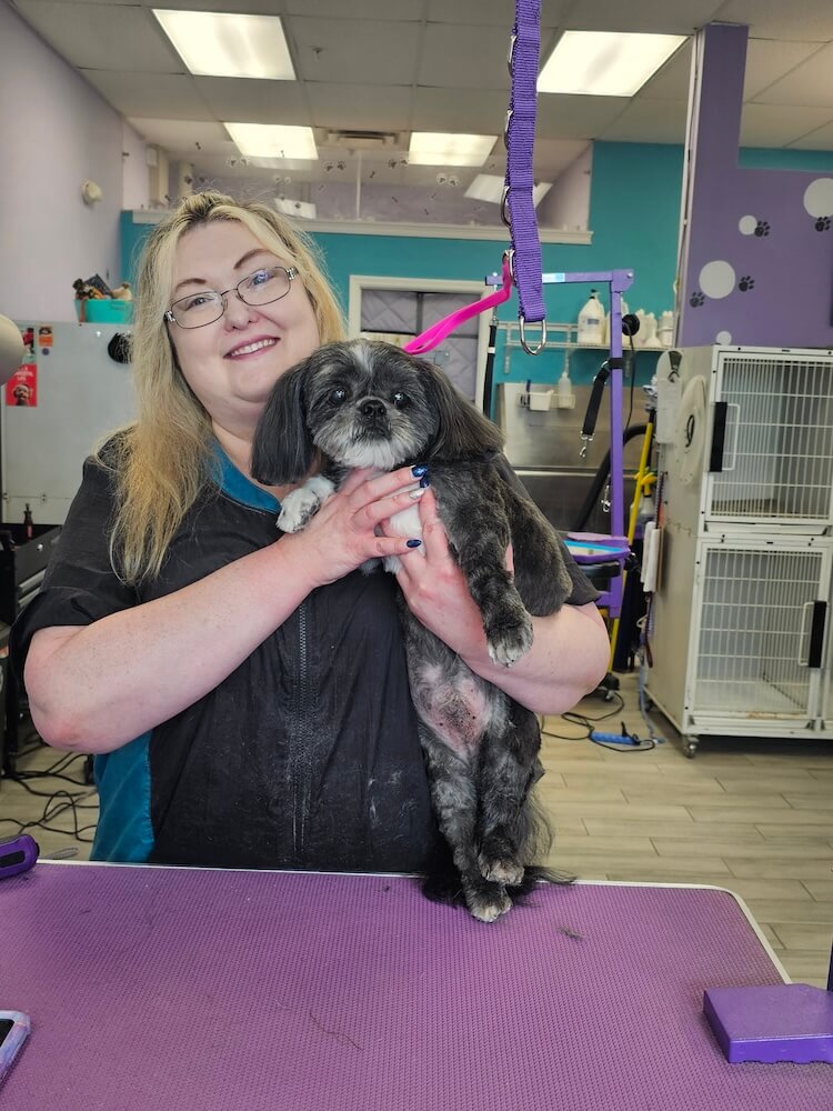 smiling groomer holding a black dog