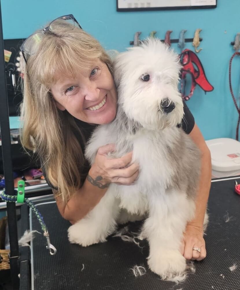 smiling groomer posing with gray and white dog